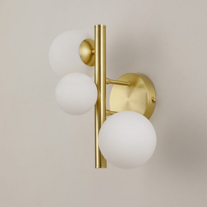 A brass wall-mounted lamp with three sphere-shaped bulbs protruding from various angles at the top, middle and bottom of the fixture.