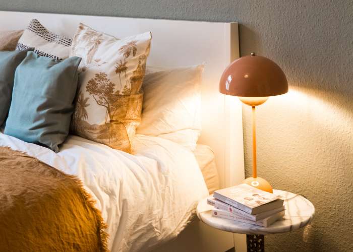 Glowing table lamp positioned next to a fluffy bed with stacked pillows