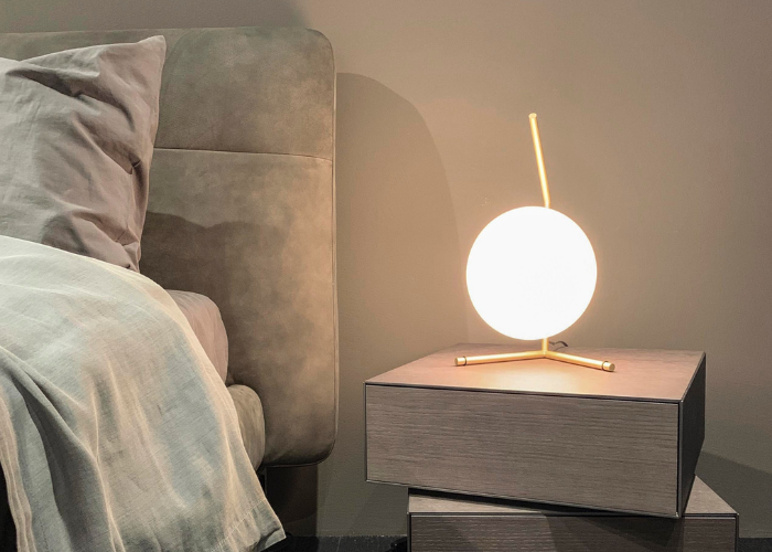 Circular globe desk lamp lit up on stacked stylish boxes next to a bed