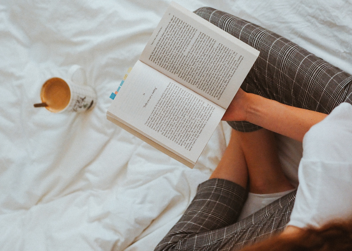 image from above of a lady holding an open book and a coffee