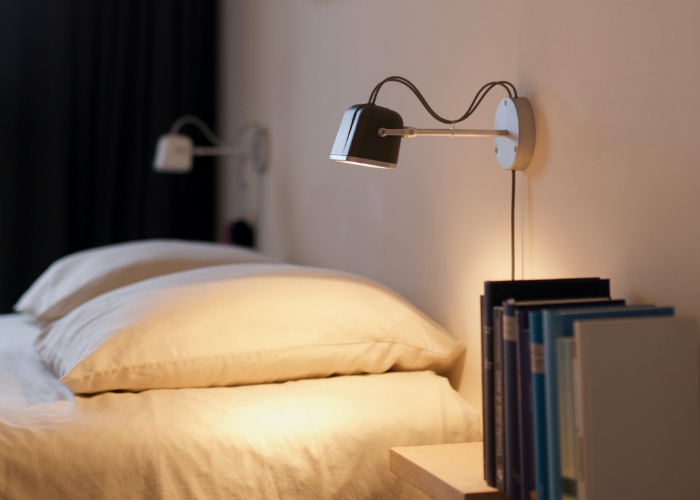 image of a bedside table, side view of bed and a wall reading light shining down