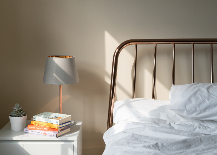 copper table light with grey shade positioned next to a bed